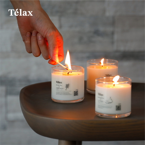 Telax　アロマキャンドル　焙じ茶×サンダルウッド 白い容器に入ったキャンドルが、焙じ茶とサンダルウッドの香りが漂う状態。