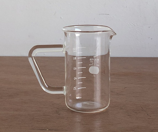 取っ手付きトールビーカー 100ml 透明なビーカーが取っ手を持ち、液体が入った状態で横に置かれている様子